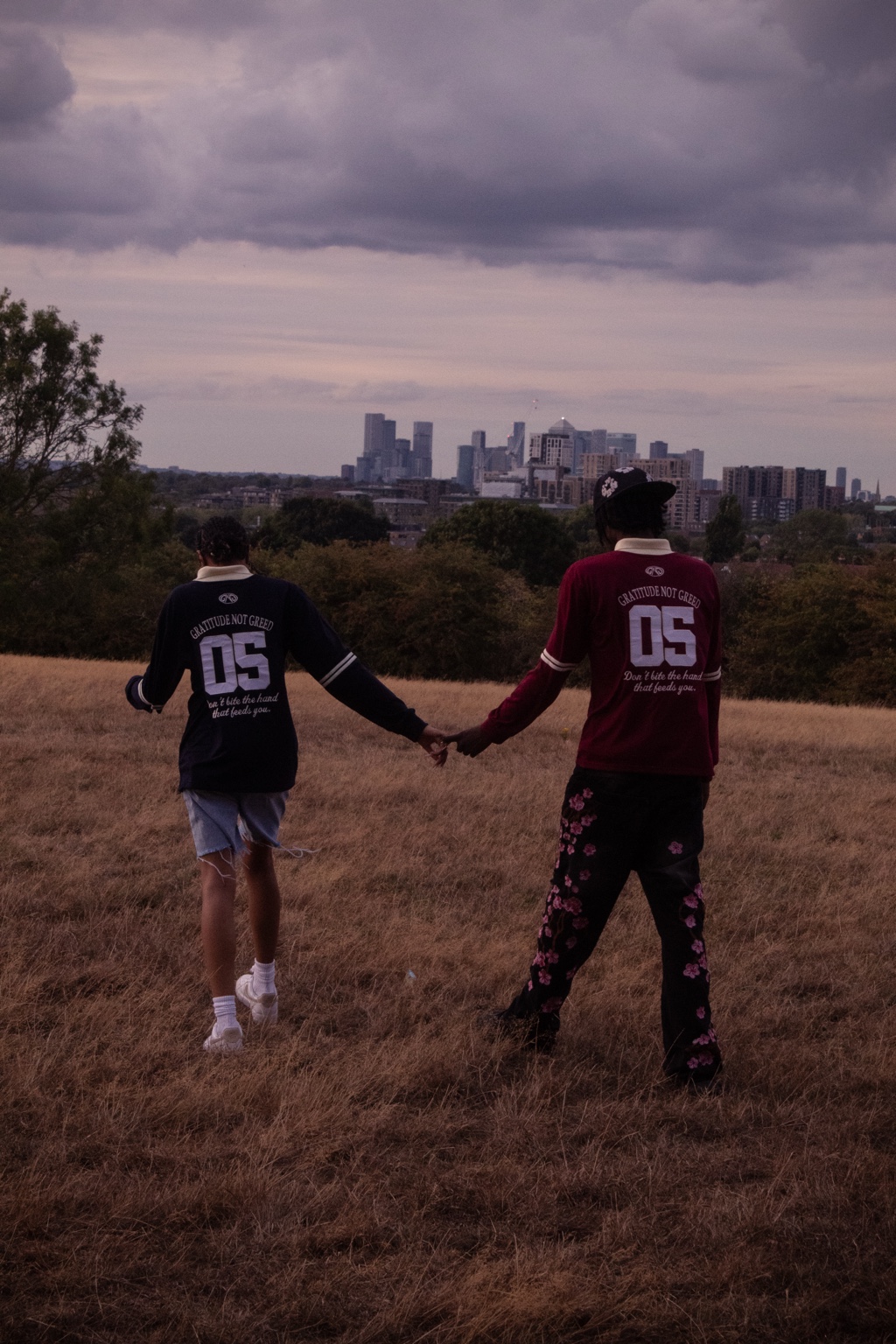 GNG campaign — two people walking hand in hand in navy and burgundy 05 rugby polos, London skyline at dusk