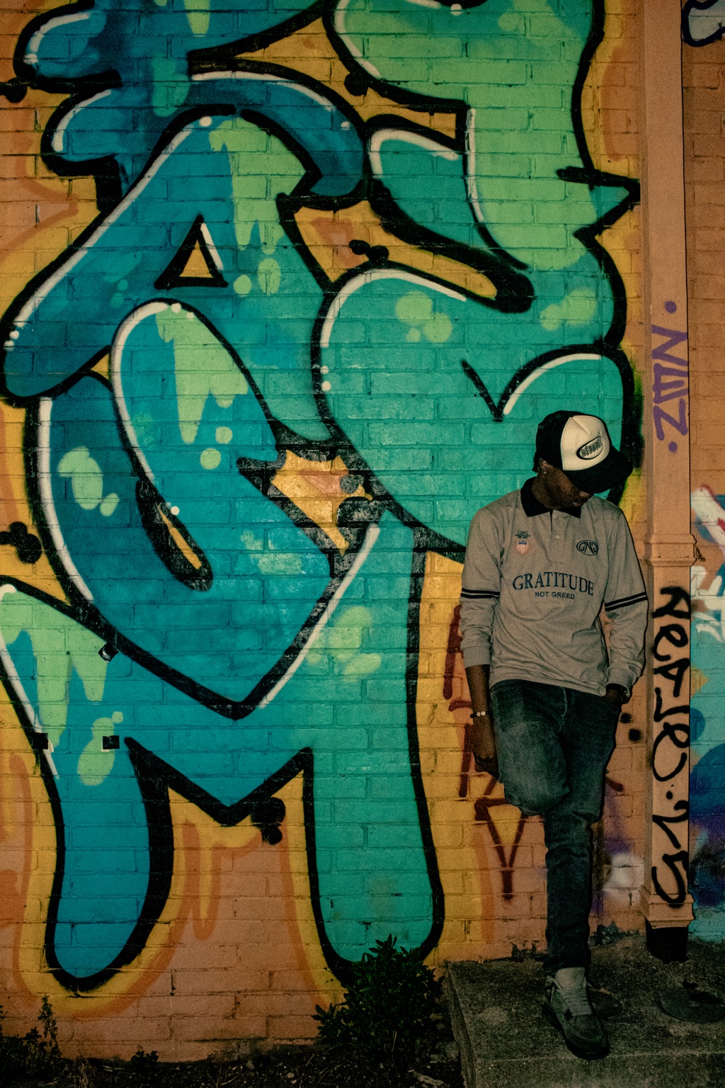 GNG campaign — grey Gratitude Not Greed rugby polo worn against a teal graffiti wall in London