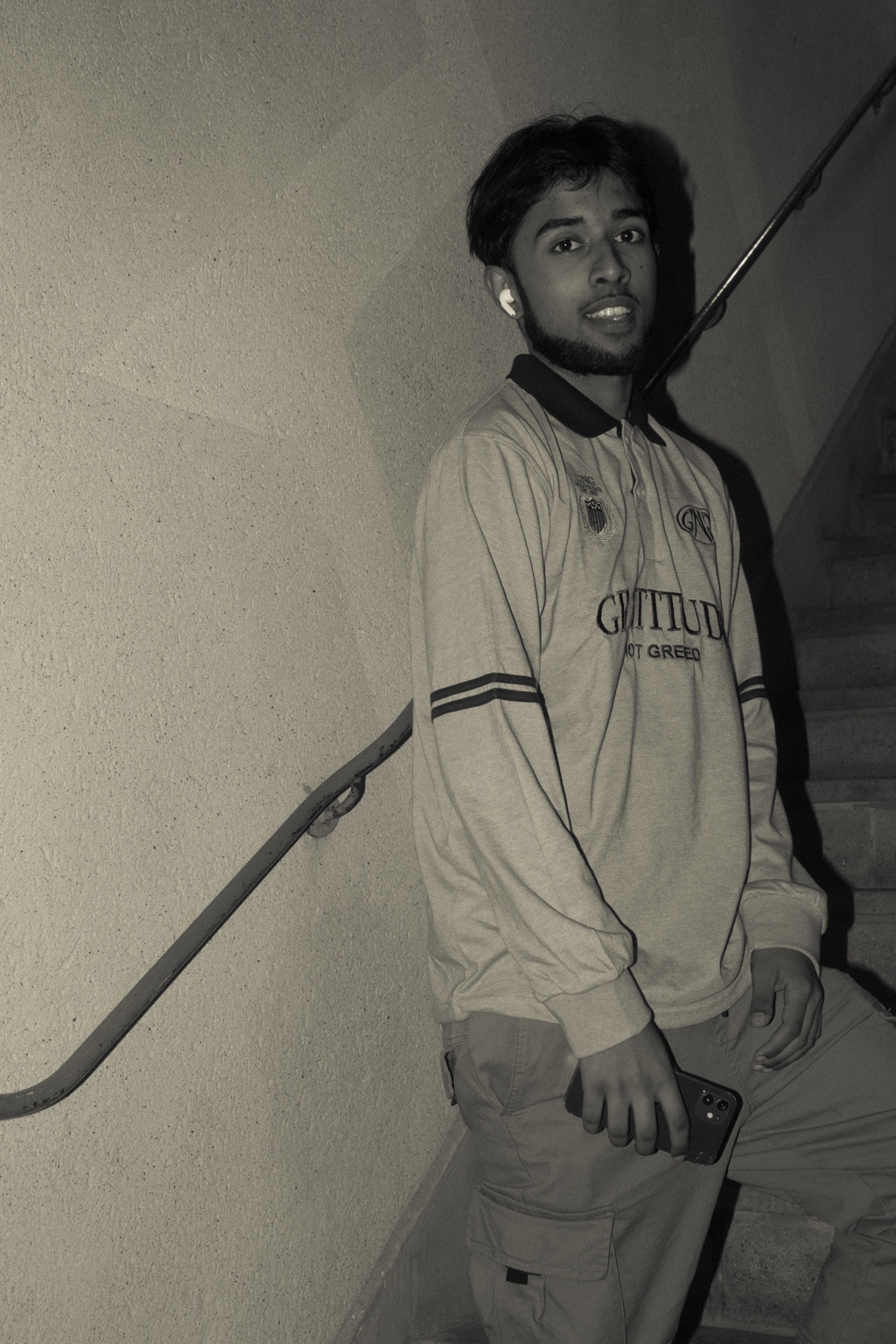 GNG campaign — grey Gratitude Not Greed rugby polo worn on a concrete stairwell, black and white